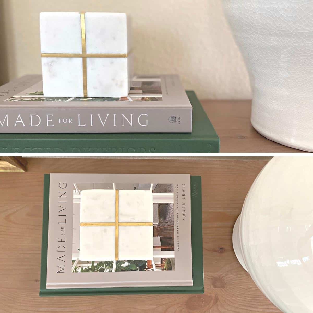 A marble and brass cube object sits atop two books; one gray and one dark green, next to a white vase