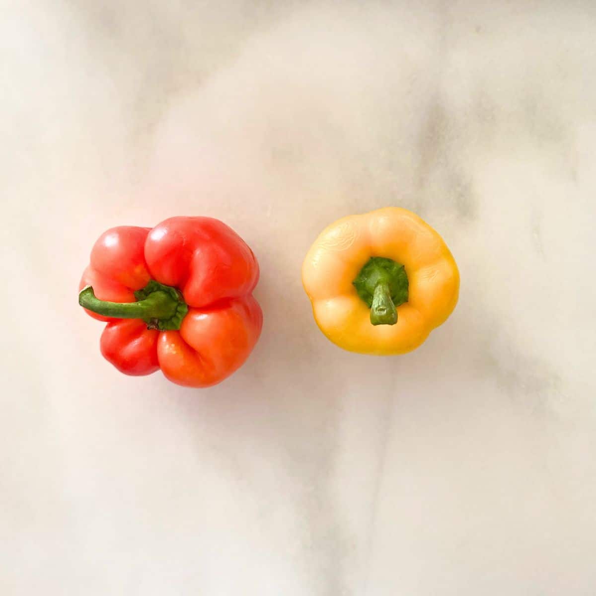 One red and one yellow fresh uncut bell pepper