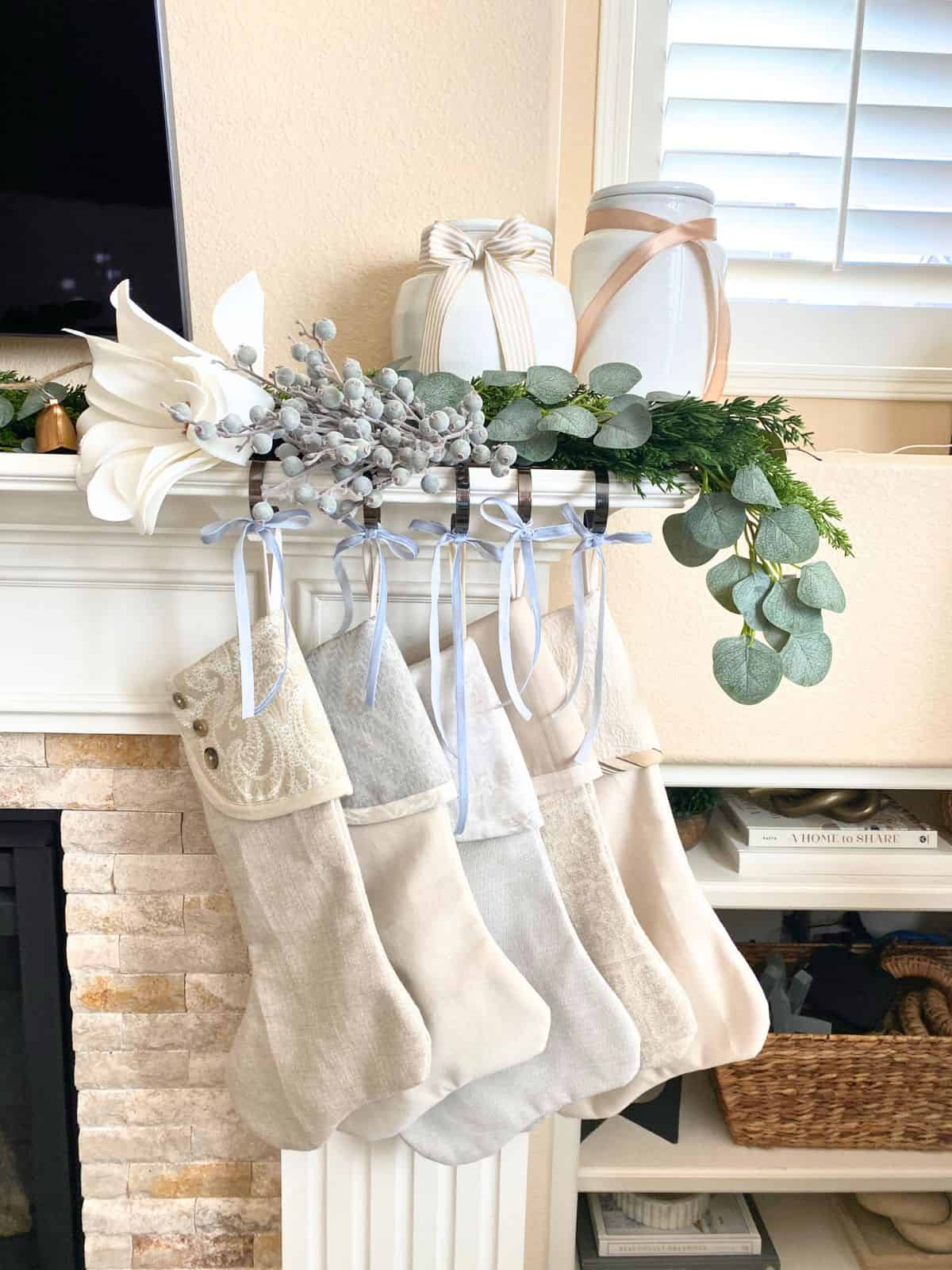 neutral stockings surrounded by garland and blue berry stems hanging on mantel