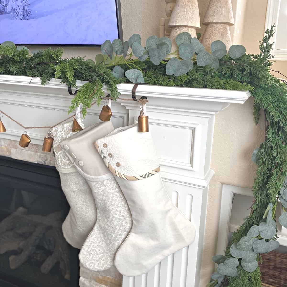 Three neutral stockings decorate a holiday fireplace mantle