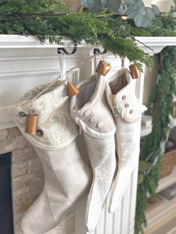Garland on mantel with three neutral stockings and metal bells