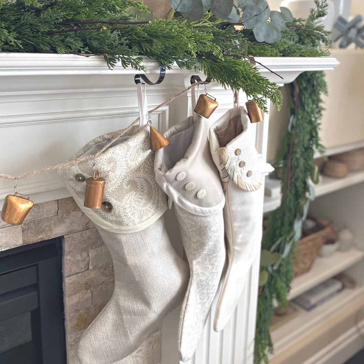 Garland on mantle with three neutral stockings and metal bells