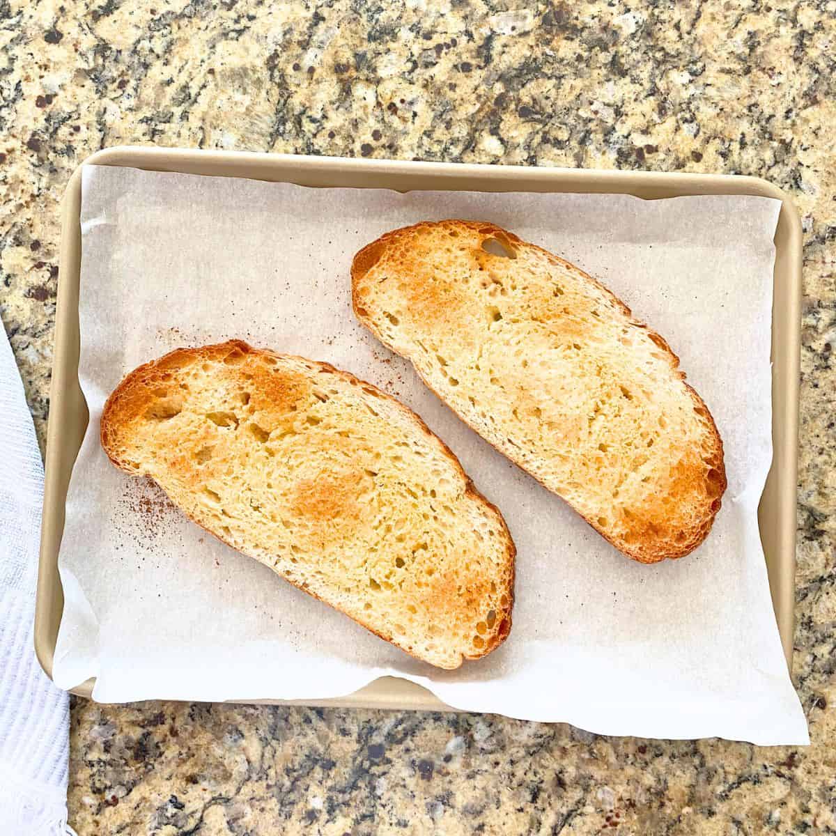 Homemade garlic toast fresh from the oven on a parchment paper lined gold baking sheet pan