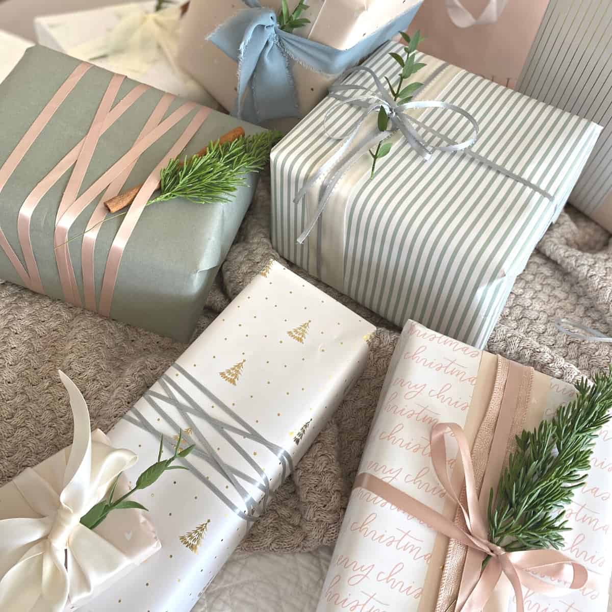 Assorted neutral pastel wrapped gifts with layers of ribbon and sprigs of greenery