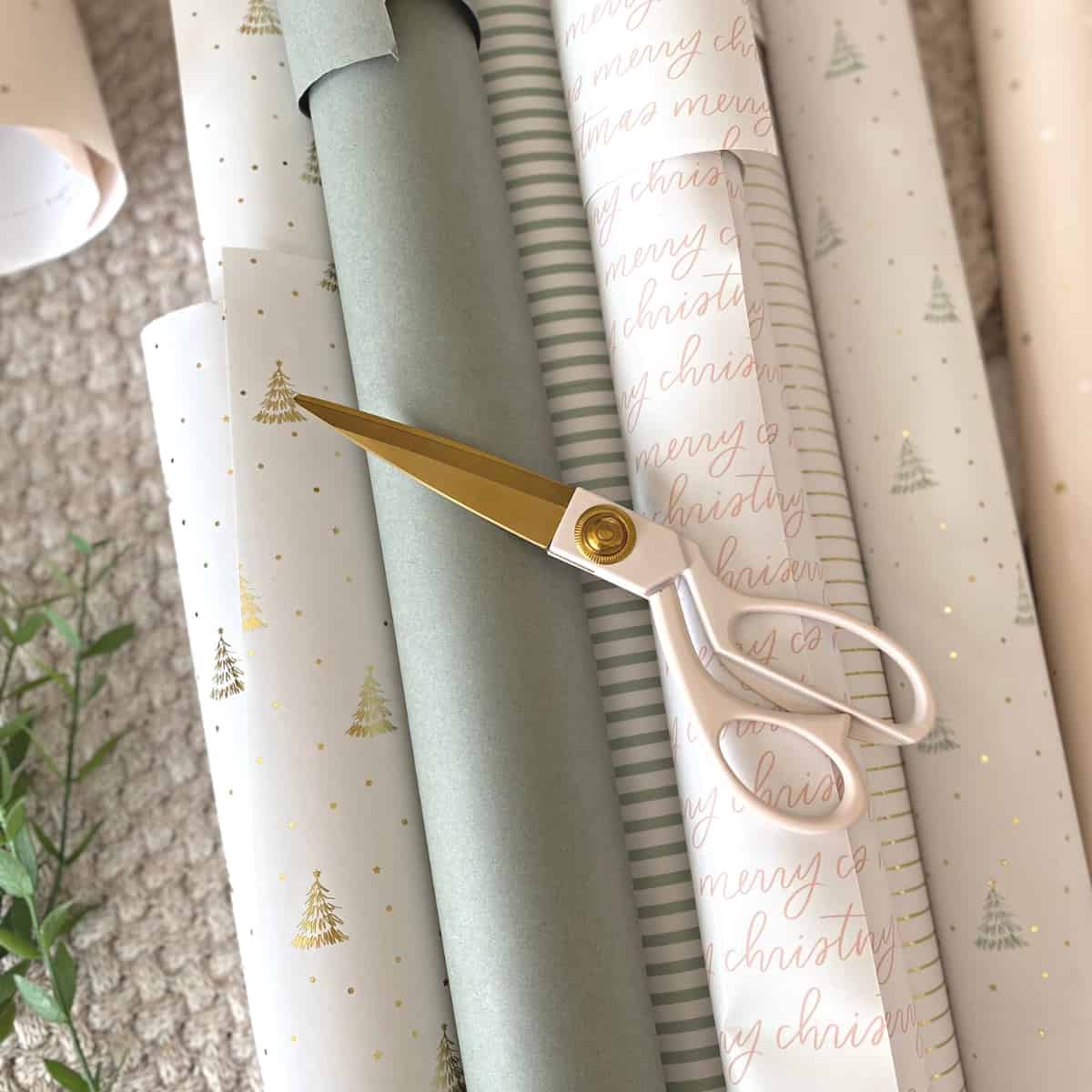 Sharp blush pink scissors atop a stack of neutral gift wrapping paper