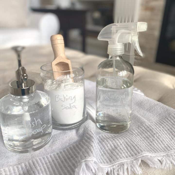 Glass soap dispenser, jar with wooden scoop and spray bottle atop a cotton hand towel