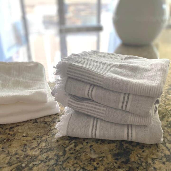 Group of three neutral Turkish cotton kitchen towels folded and stacked on top of a granite countertop