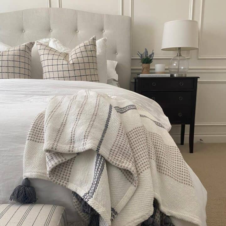 guest bedroom taken from the end of the bed, showing white organic cotton bedding, a striped throw blanket, and a dark wood nightstand