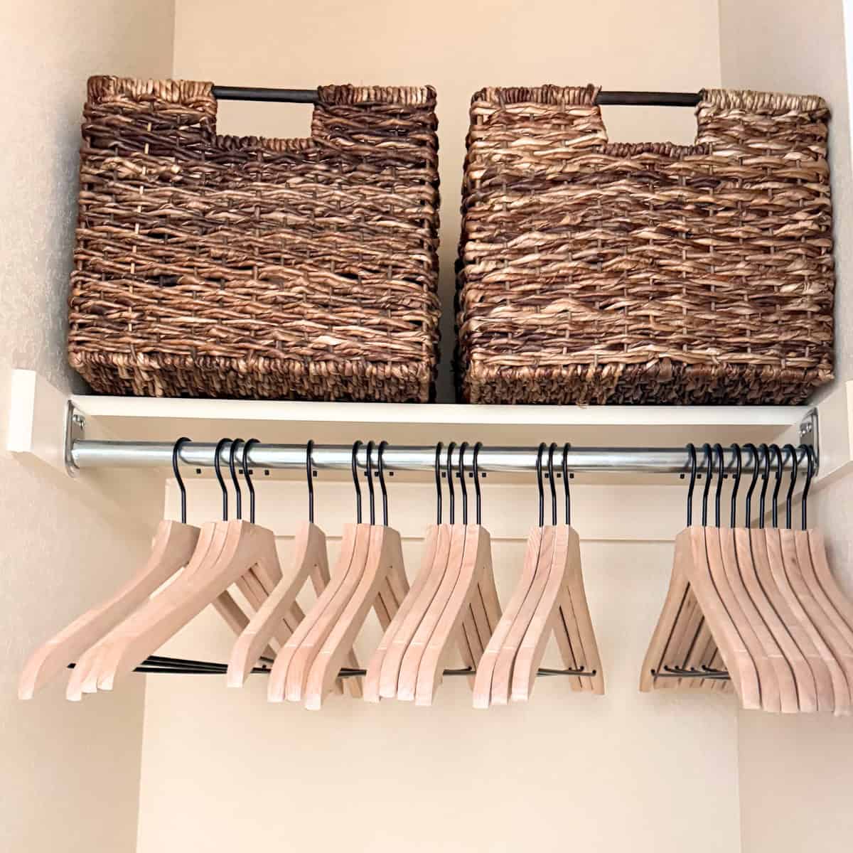 empty hangers in a closet with dark rattan baskets above on a shelf