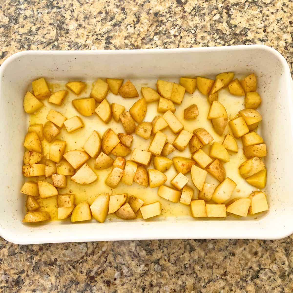 Raw buttered and seasoned yellow potatoes in a Pillivuyt porcelain rectangular roaster pan