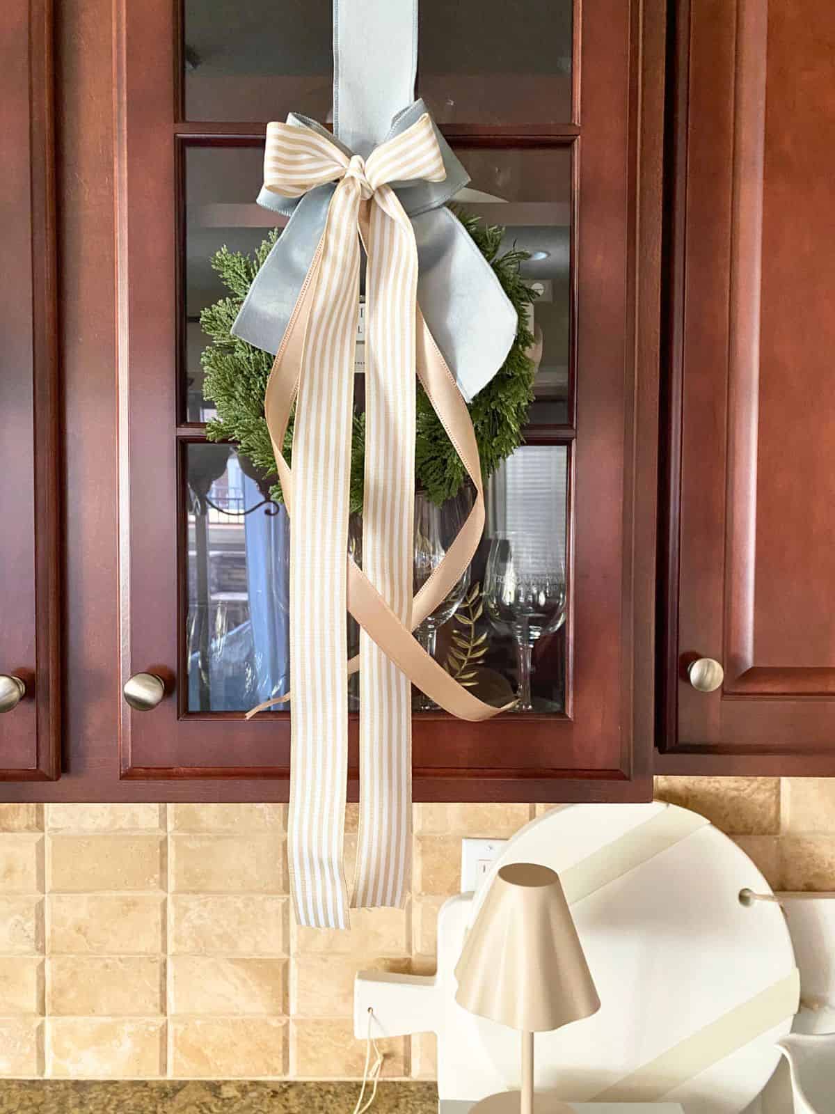 wreath decorated with taupe and blue ribbon hanging on glass cabinet door