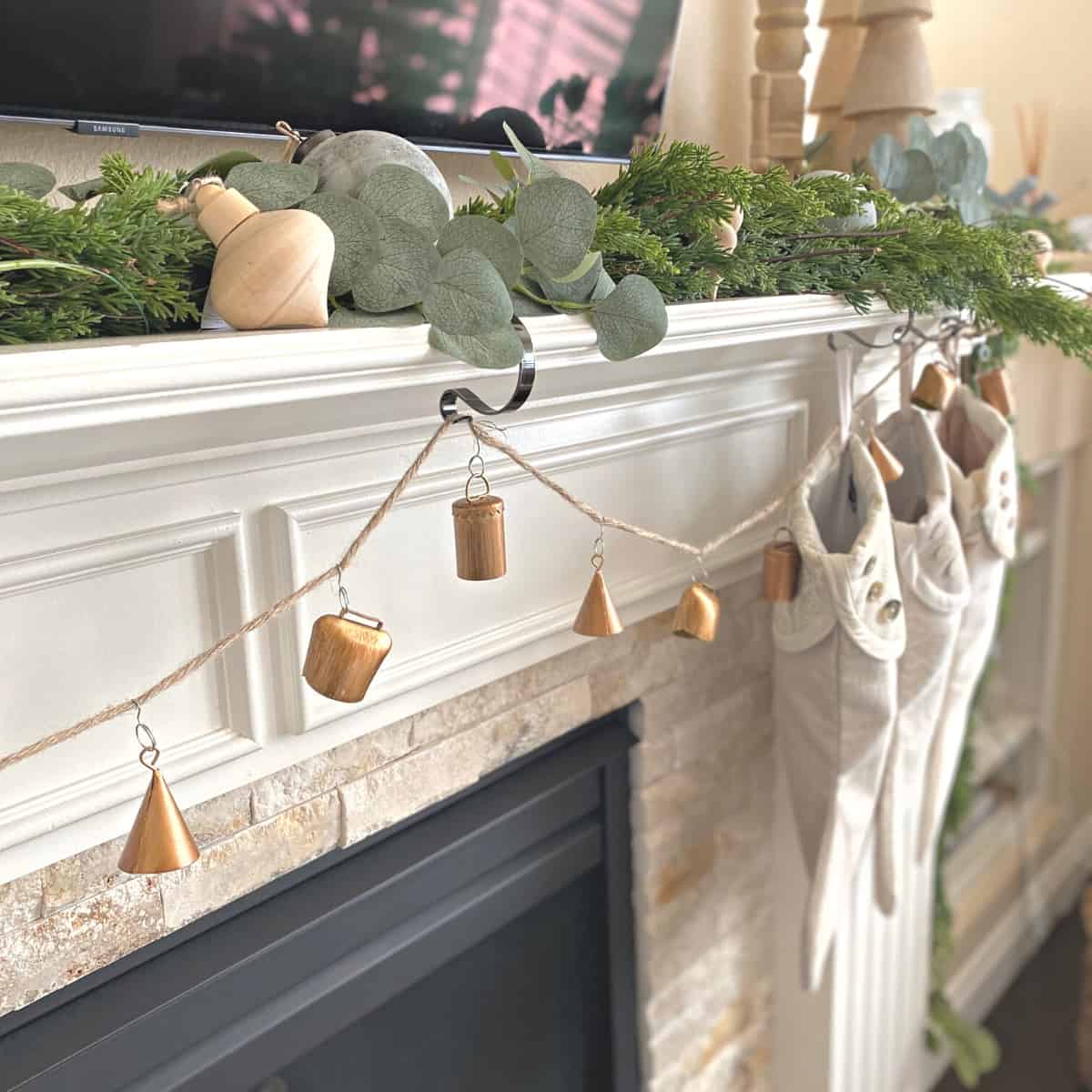 Fireplace mantel decorated for Christmas with greenery garland, metal bell garland and stockings