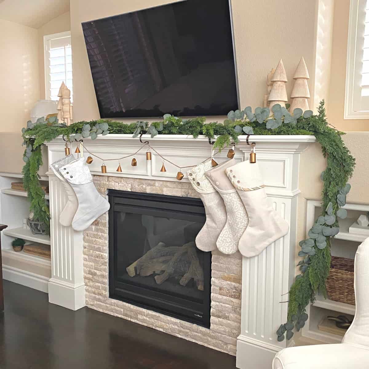 Fireplace mantle decorated with holiday garland, stockings and metal bells