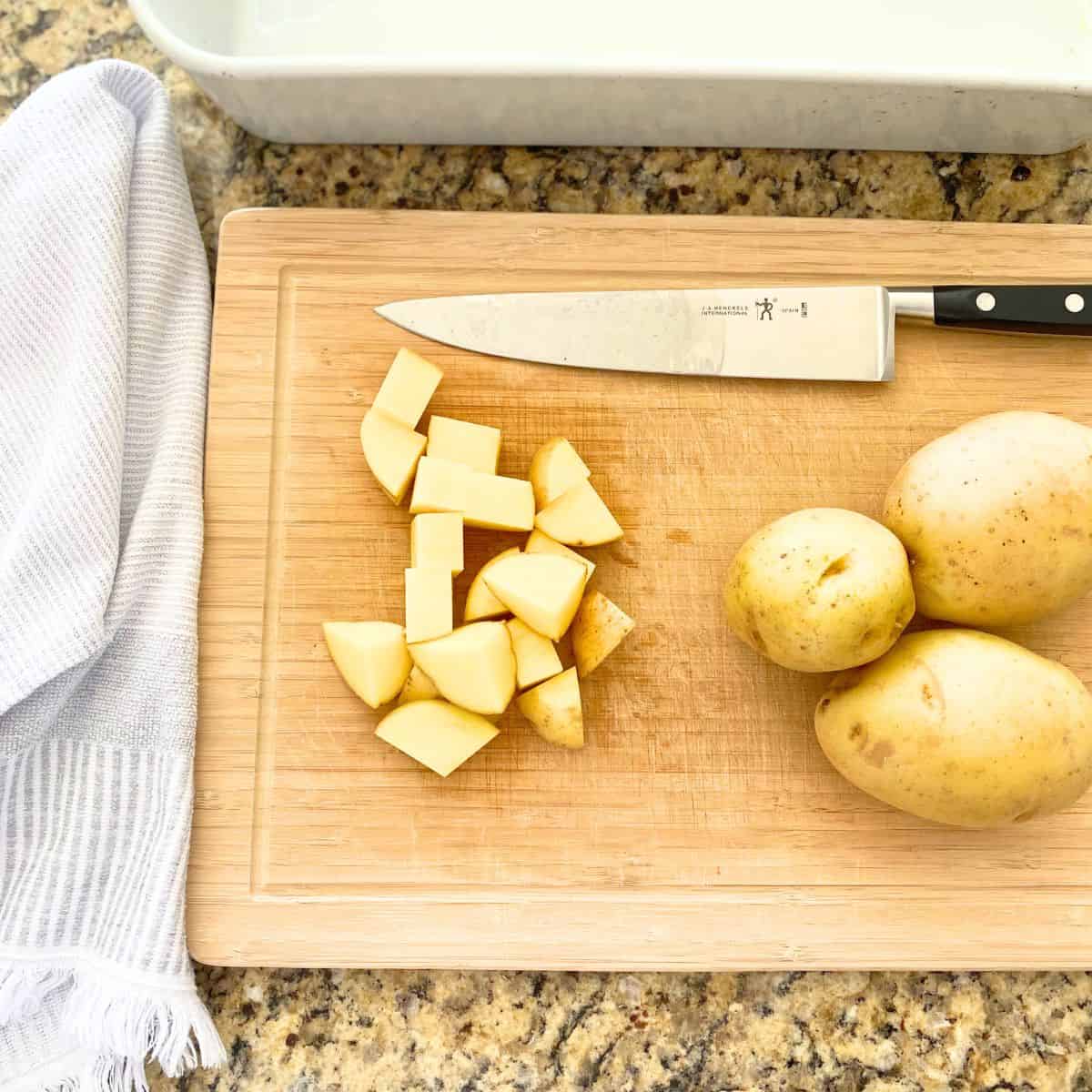 One cubed raw yellow potato atop a cutting board