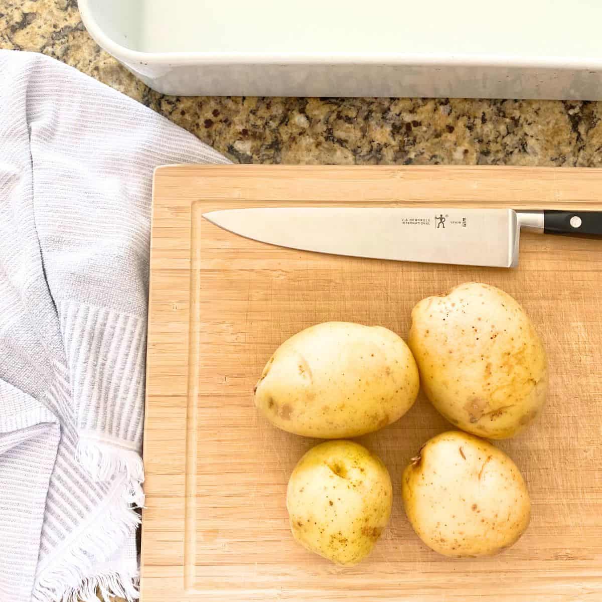 Four whole raw yellow potatoes atop a cutting board