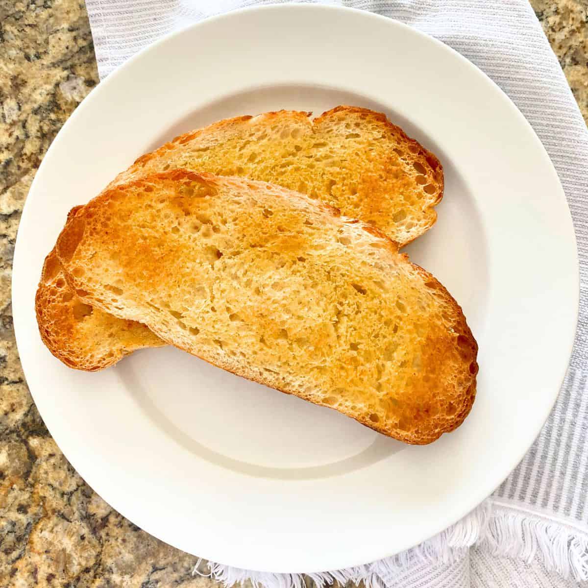 Homemade garlic bread roasted in the oven on a white dinner plate from above