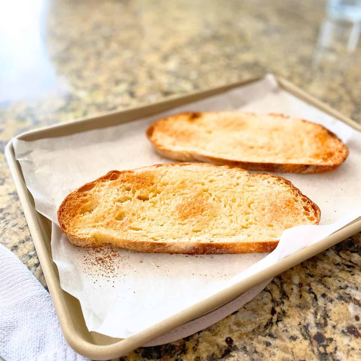 Homemade garlic toast fresh from the oven on a parchment paper lined gold baking sheet pan