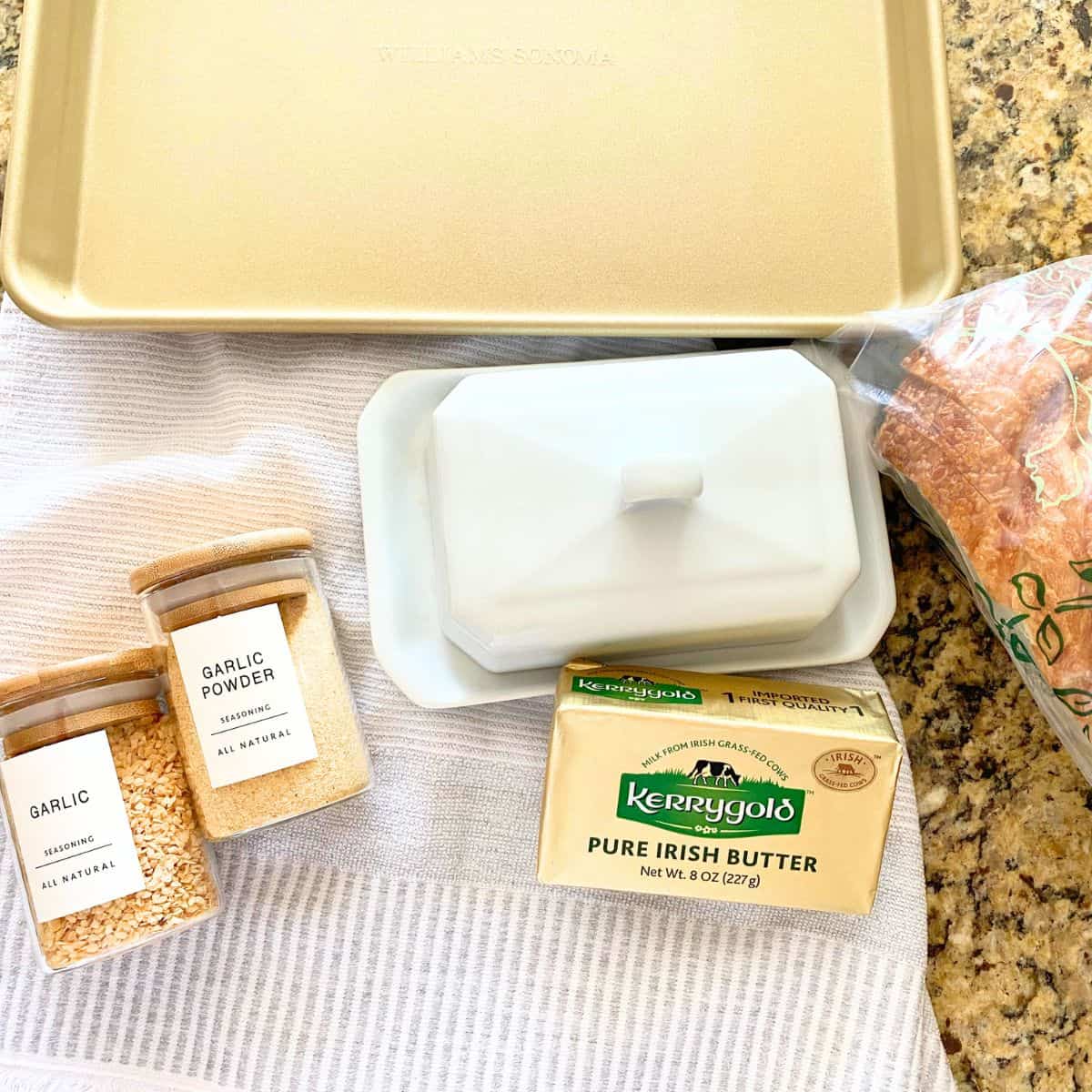 Ingredients for homemade garlic bread, consisting of garlic powder, butter, bread and a gold baking sheet pan