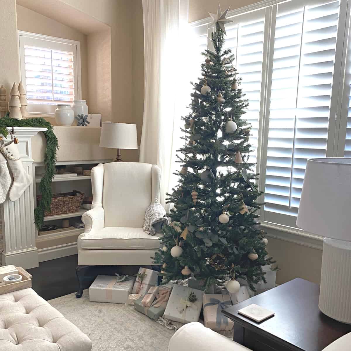 A decorated Christmas tree with neutral ornaments placed in the front window of a living room