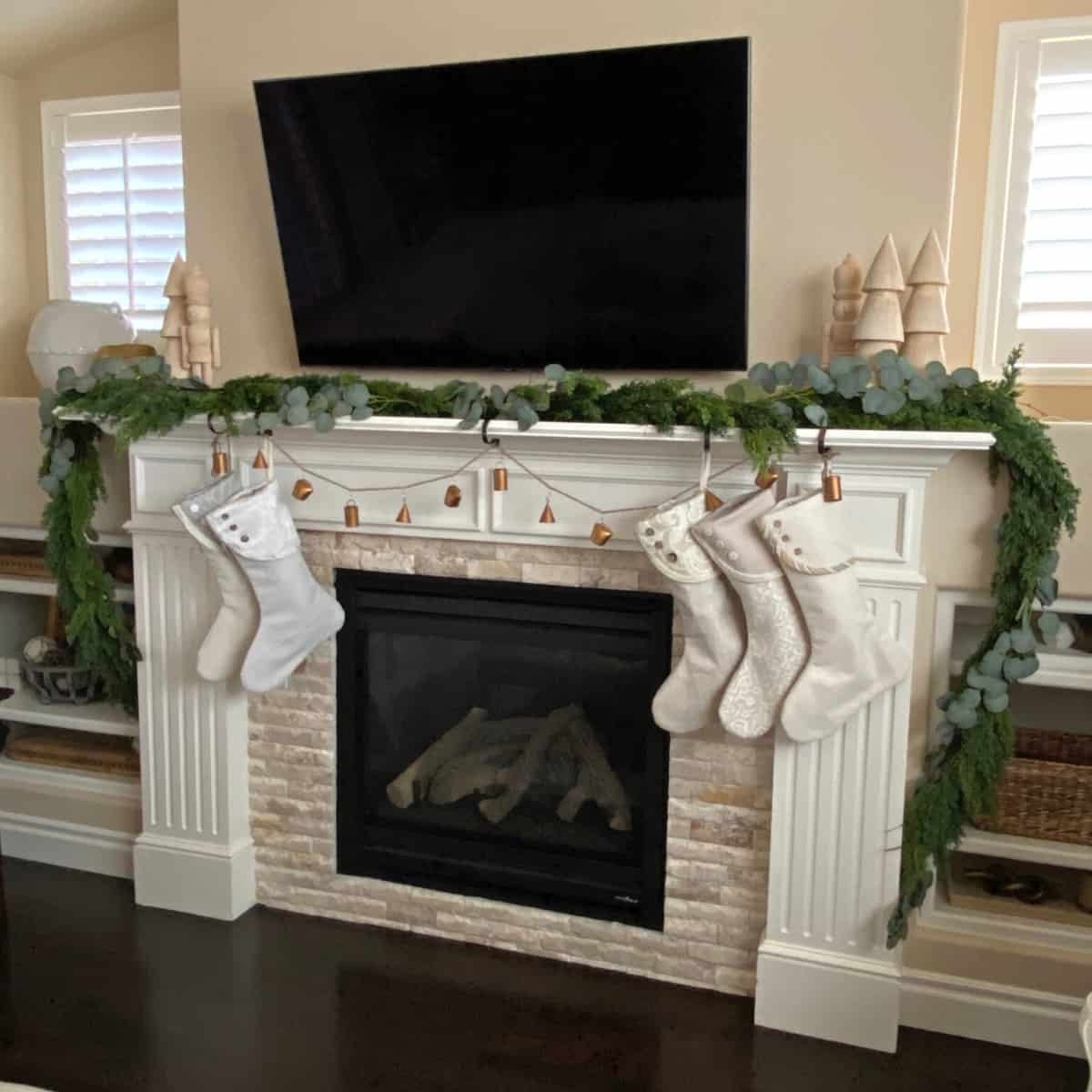 Fireplace mantle decorated with holiday garland, stockings and metal bells