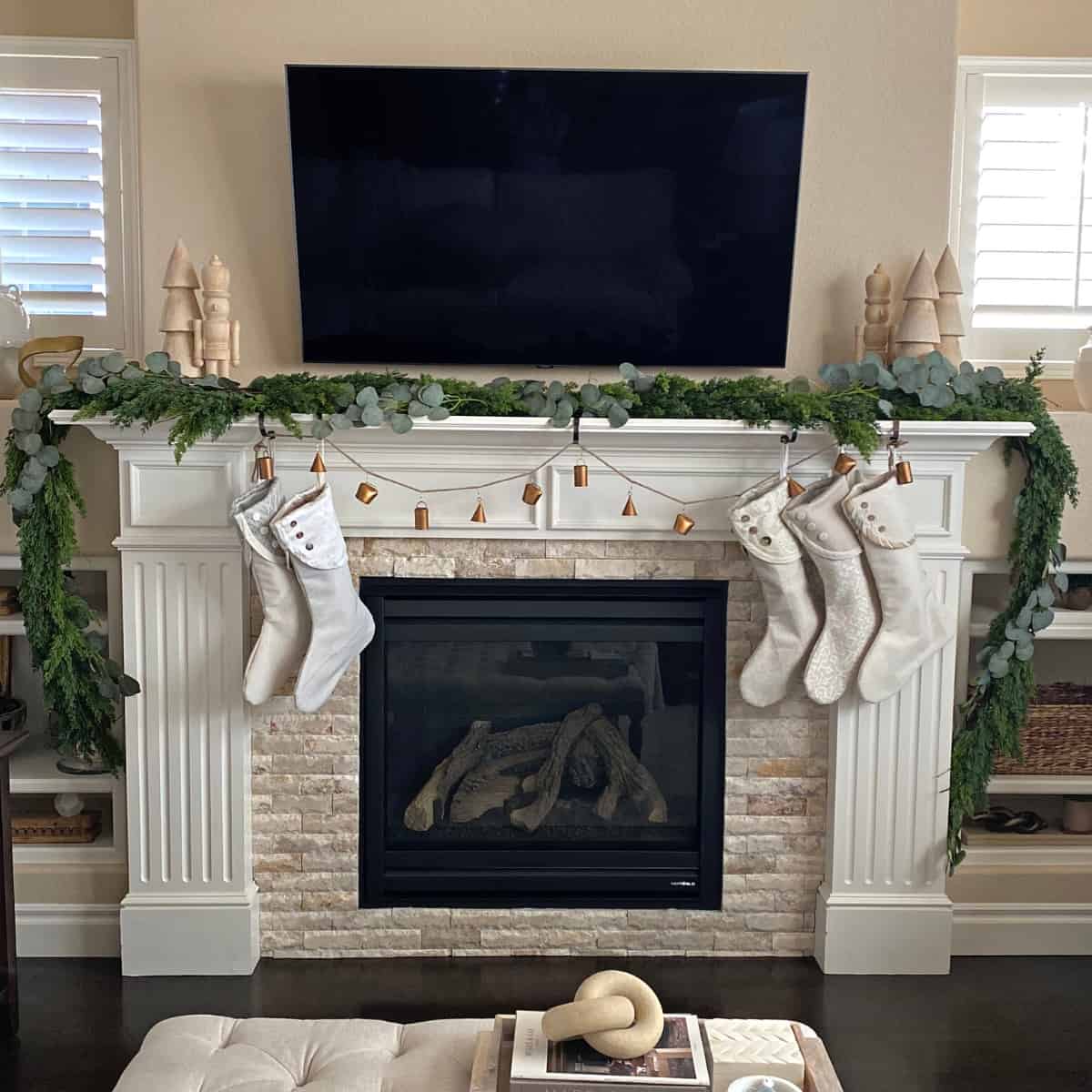 Fireplace mantel decorated with holiday garland, stockings and metal bells