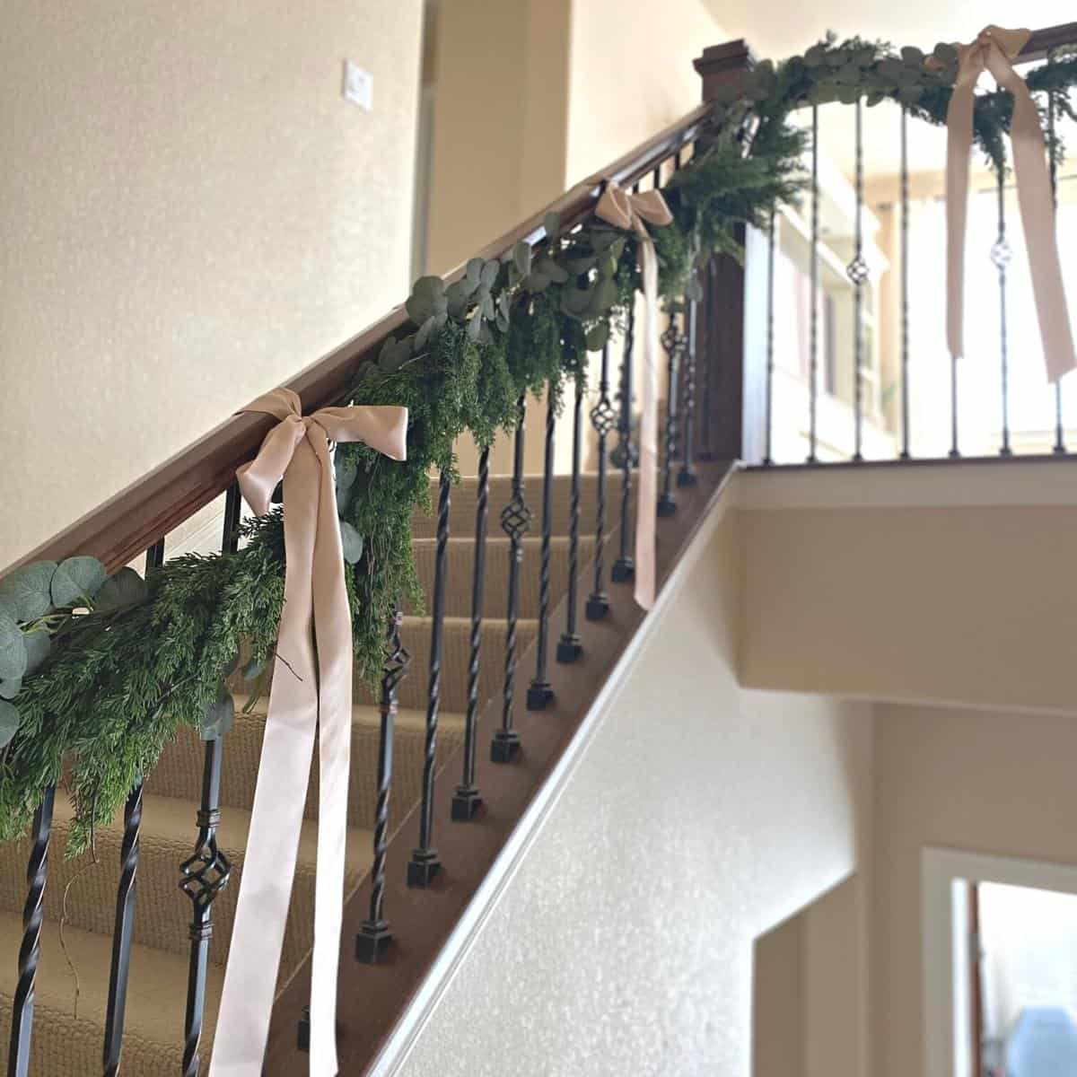 Christmas holiday garland, of faux cedar and eucalyptus, on stairs with taupe-pink ribbon bows