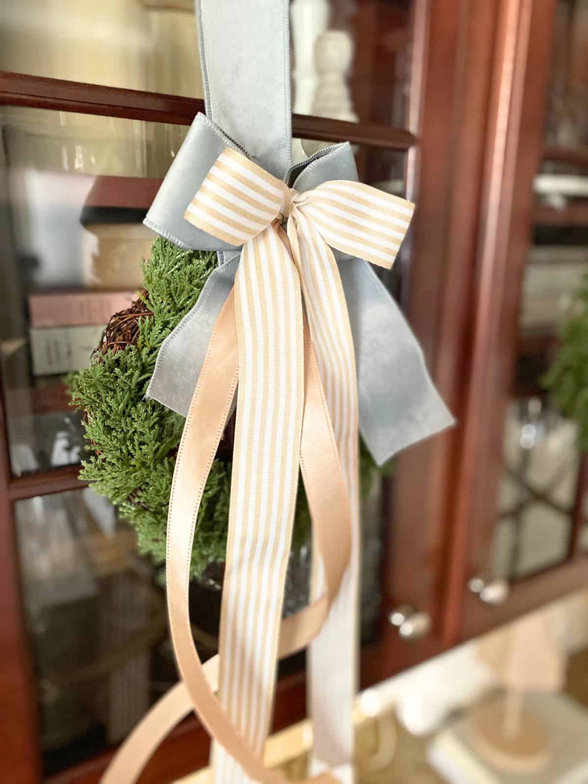 wreath decorated with taupe and blue ribbon hanging on glass cabinet door