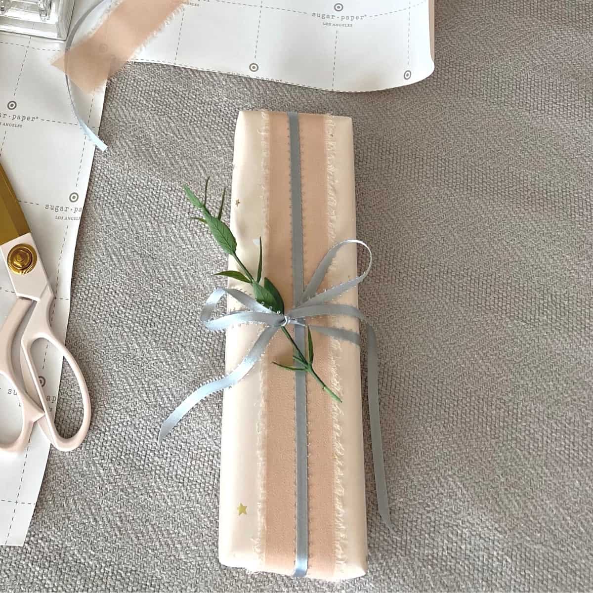 Gift wrapped in pink paper layered with link chiffon ribbon under blue satin ribbon and a topper sprig of greenery