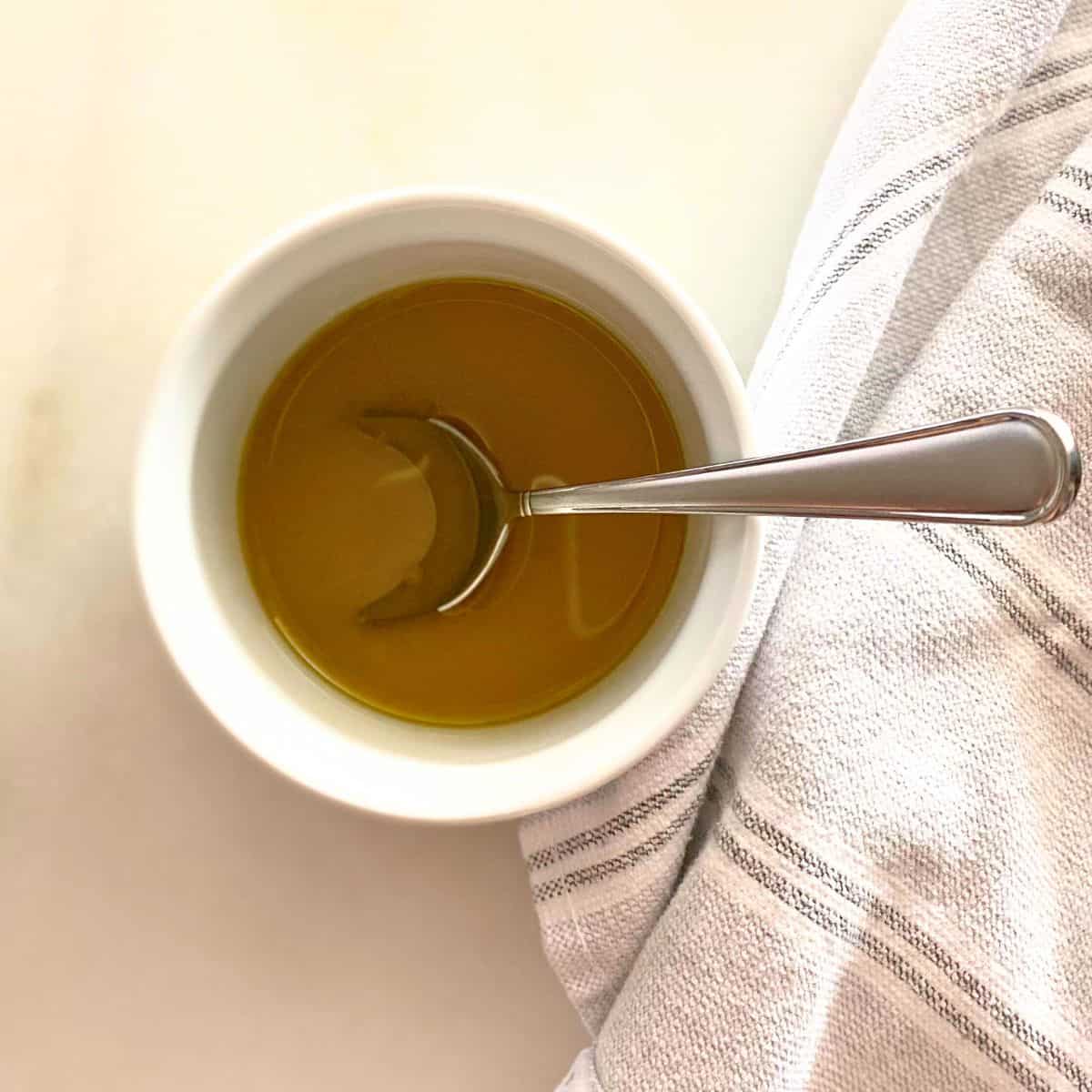 Top view of lemon olive oil dressing in a white ramekin with a stainless steel soup spoon