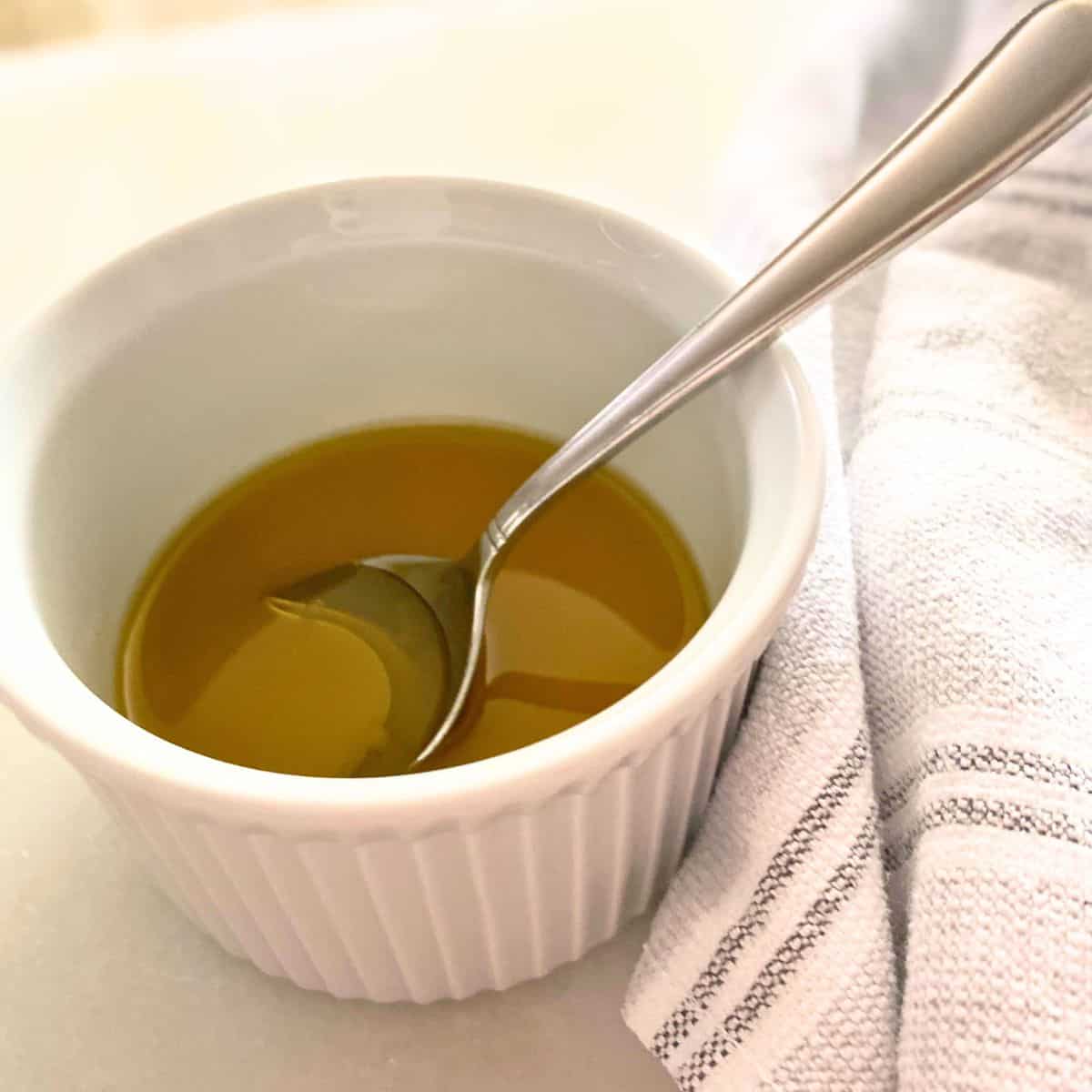 Lemon olive oil dressing in a white ramekin with a stainless steel soup spoon