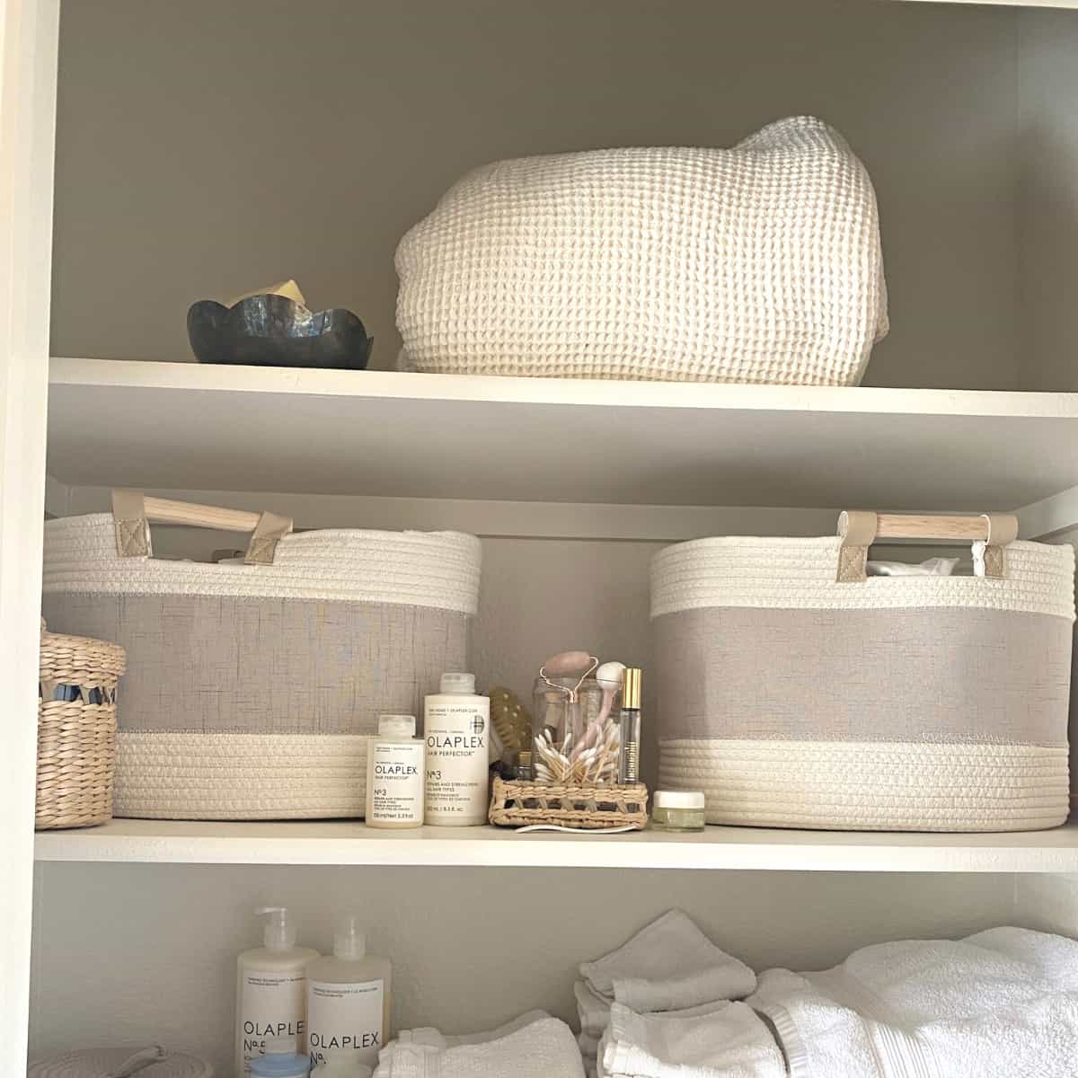 Bed linens and cotton rope baskets stored with toiletries in a closet