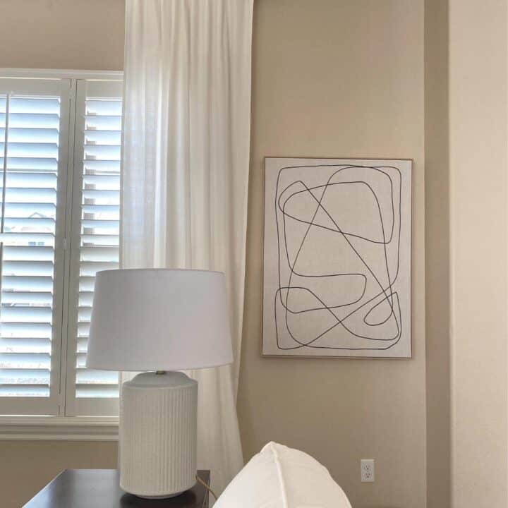 bright, neutral painted living room of a window, off-white curtains and the Middle of Nowhere Passage artwork. A table lamp sits on a side table.