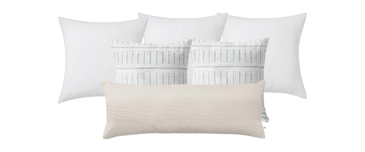 Set of throw pillows for a king size bed. Three all white euro pillows in the back, two twenty-four inch square blue lined print patterned pillows in the middle and an oversized lumbar pillow in a taupe textured stripe in the front.