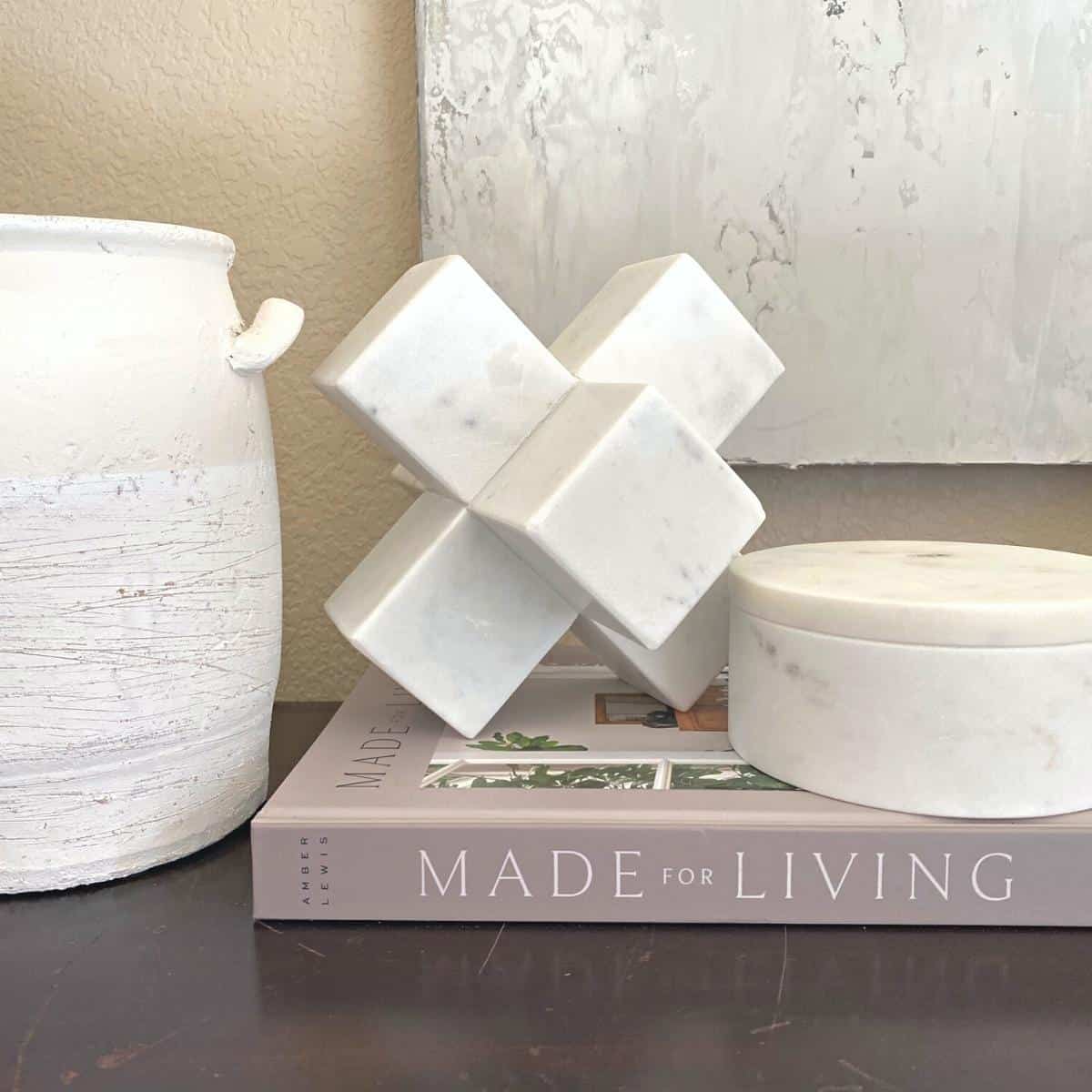 Console table styled with a white vase, marble objects on top of a book and next to two stacked boxes.