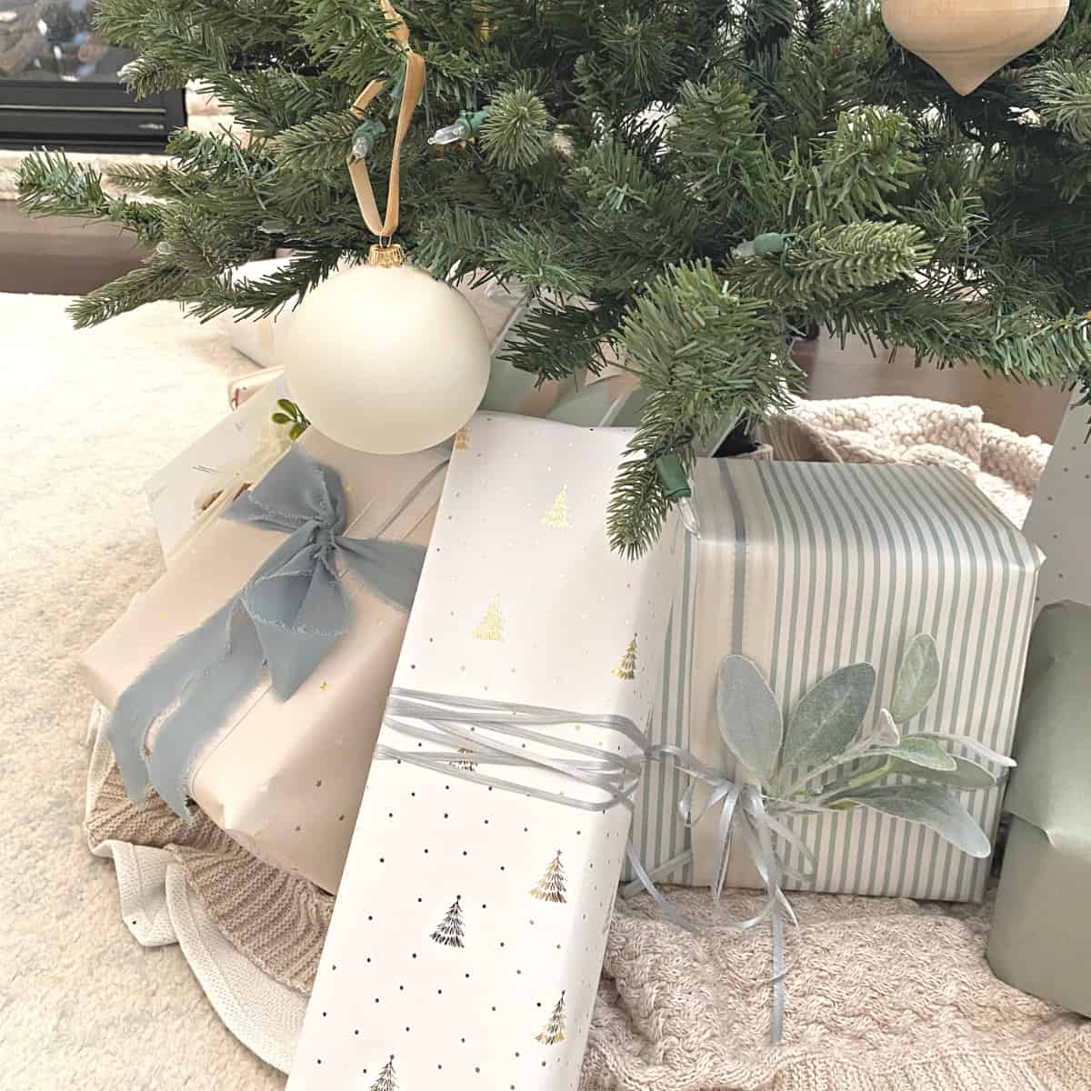 Christmas presents under a tree in neutral wrapping paper with sprigs of green and textured ribbons