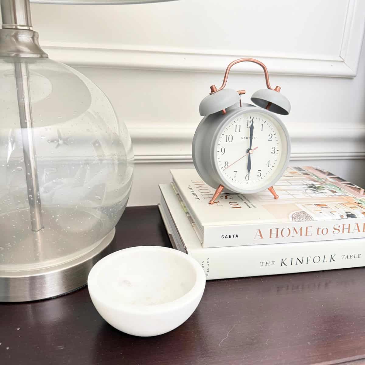 small marble dish atop a nightstand next to a lamp and alarm clock on top of two books