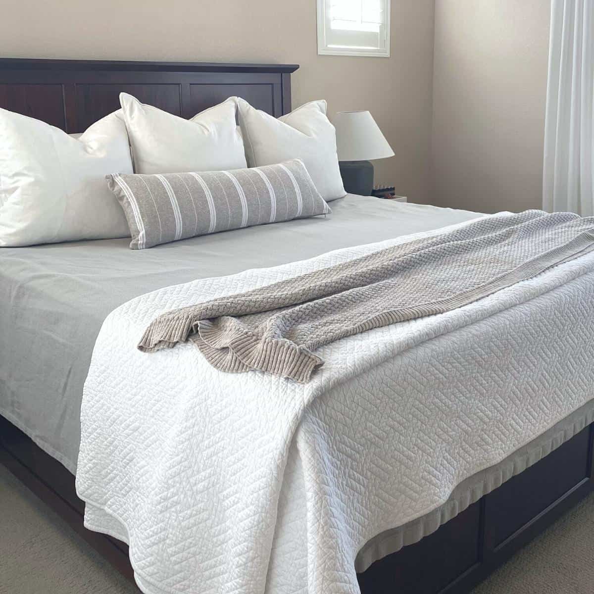 King bed with grey herringbone blanket underneath a white diamond patter coverlet and heathered brown blanket