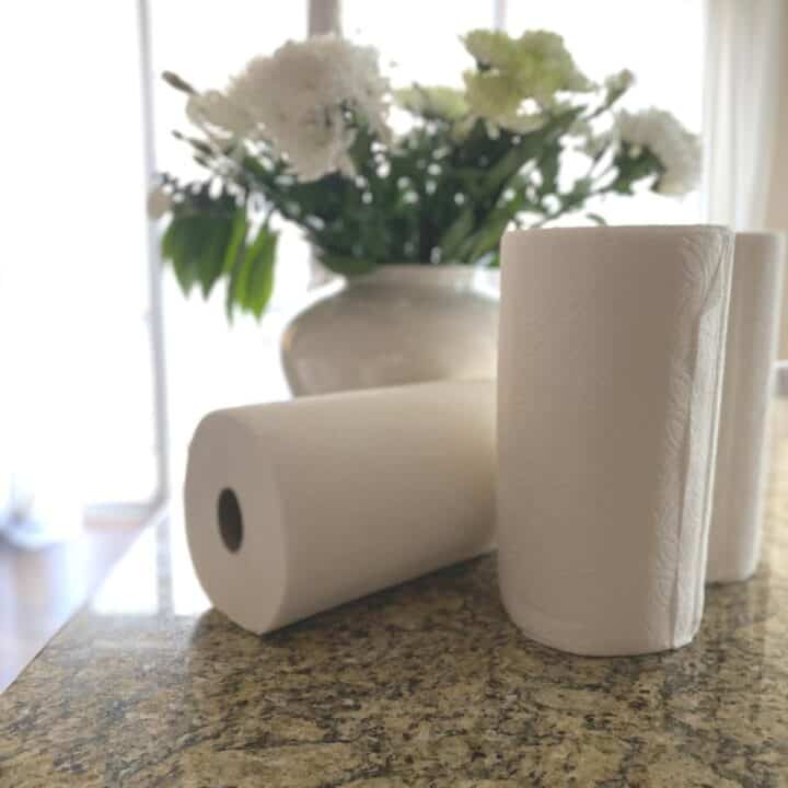 Three paper towel rolls lying on a brown granite kitchen countertop, with a vase of white flowers in the background.