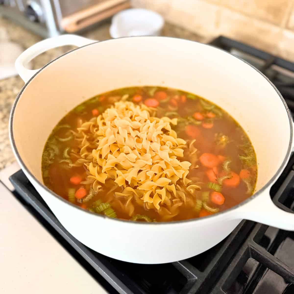 dry egg noodles added to pot of chicken noodle soup