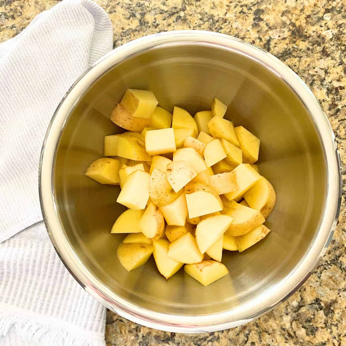 Raw yellow potatoes in a stainless steel mixing bowl