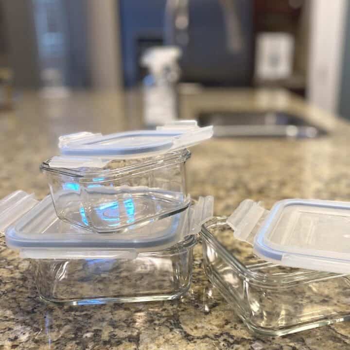 Reusable square glass containers with silicone lids stacked on a brown mottled granite countertop.