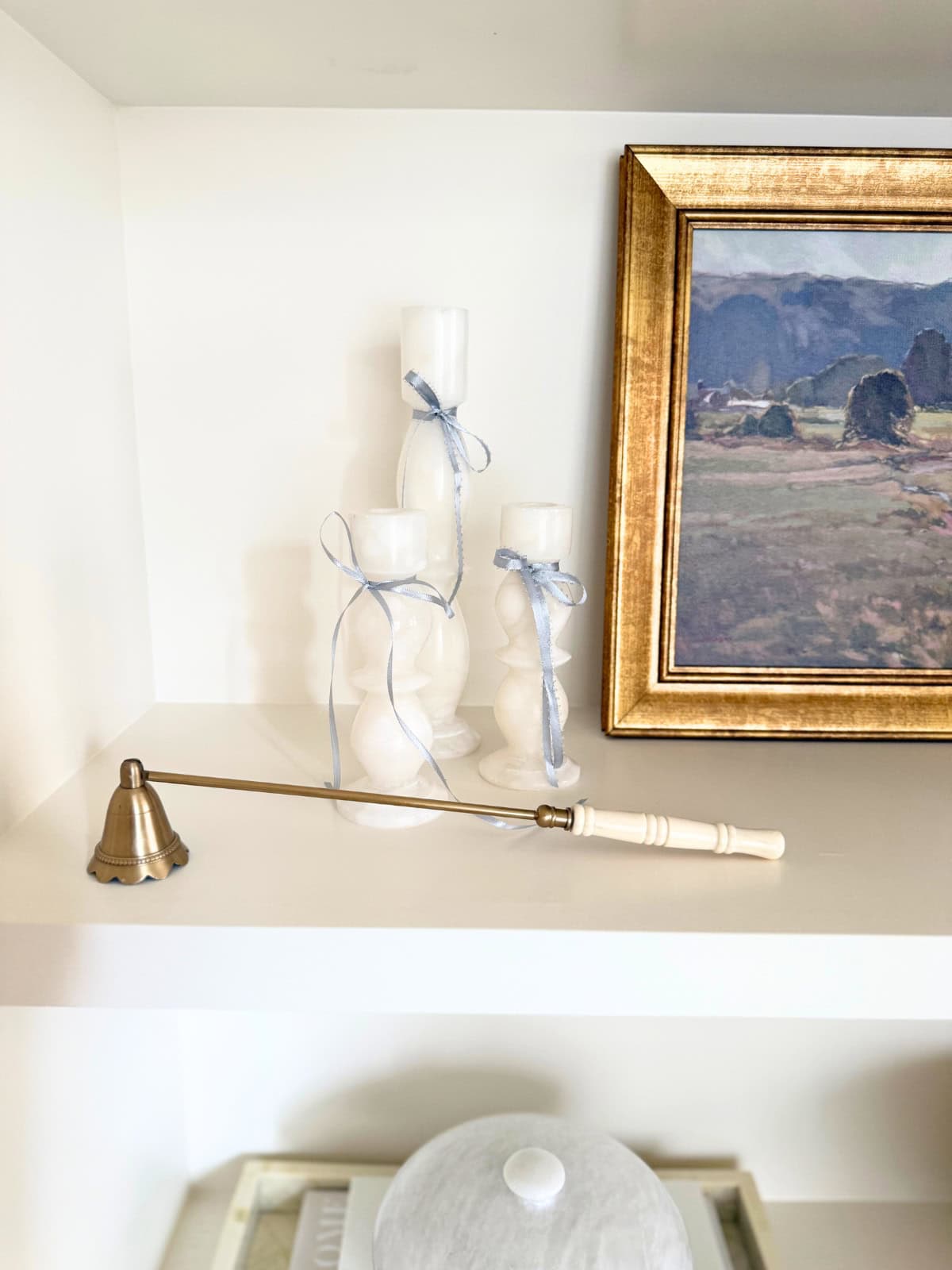 marble candlesticks with light blue ribbon bows and a snuffer next to art
