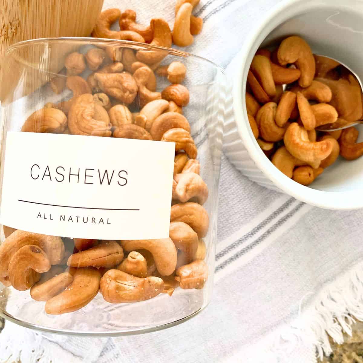 Roasted cashews served in a white ramekin next to a glass jar with a white label and the word cashews