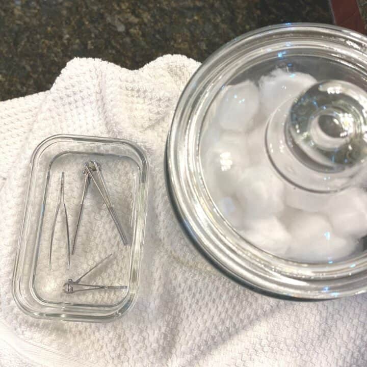 Taken from above, a small rectangular glass container with tweezers and nail clippers, soaking in rubbing alcohol to disinfect the items.