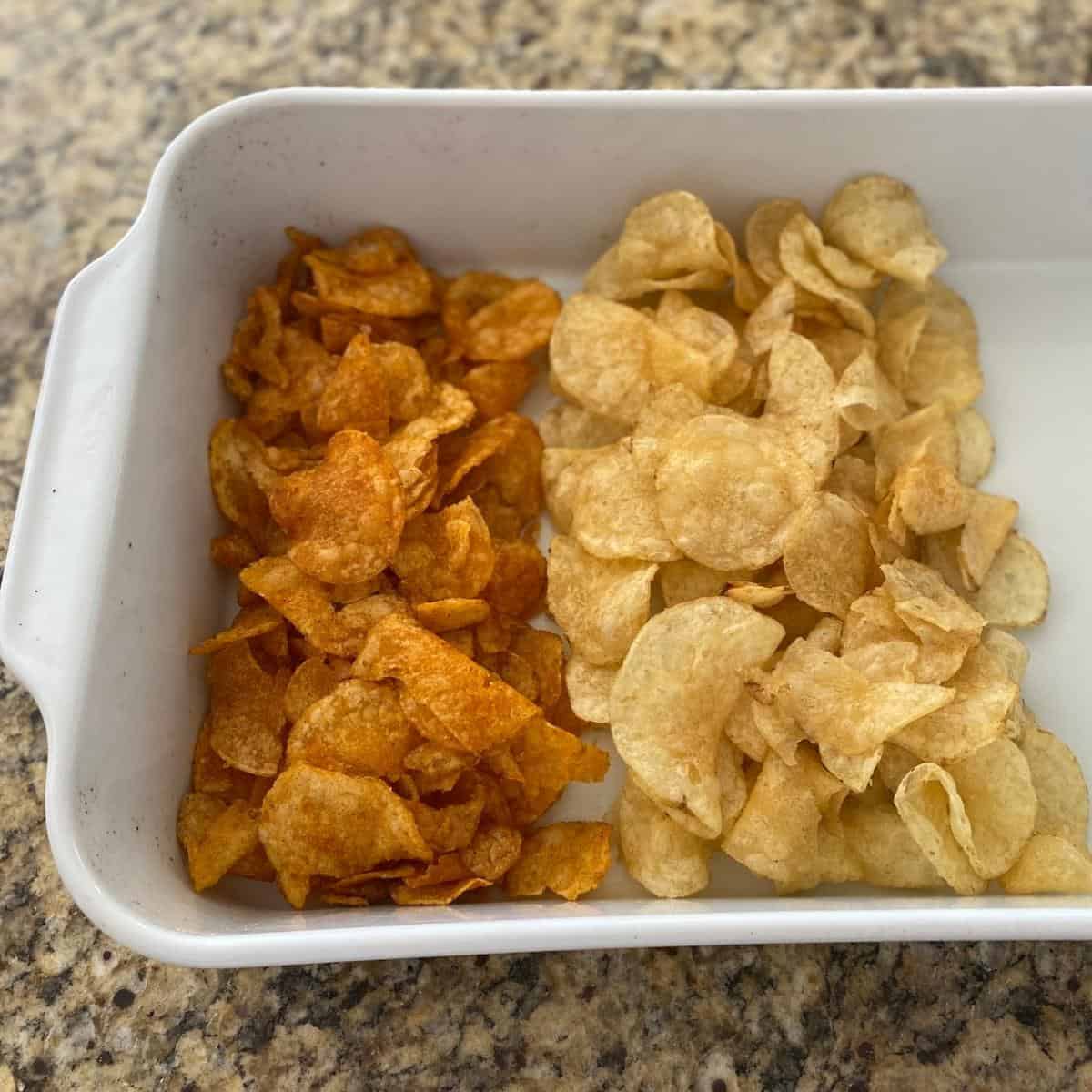 Two different flavors of potato chips served in two thirds of a white rectangular roasting pan