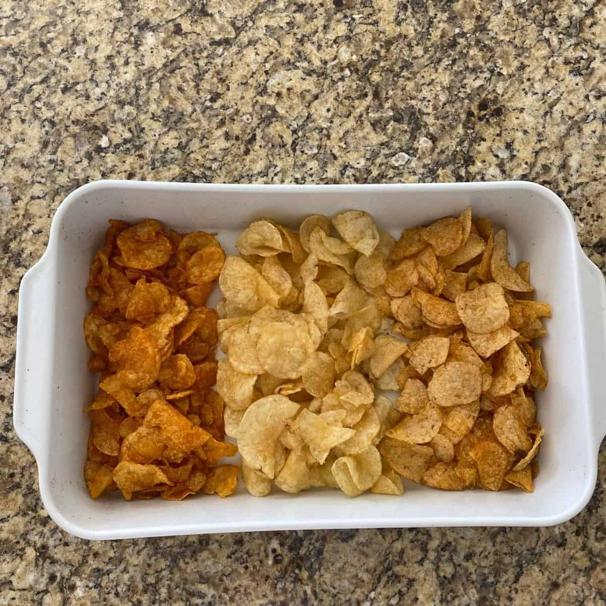 Three different flavors of potato chips served in a white rectangular roasting pan from above