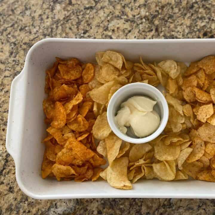 Three different flavors of potato chips served in a white rectangular roasting pan with a ramekin for chip dip in the middle