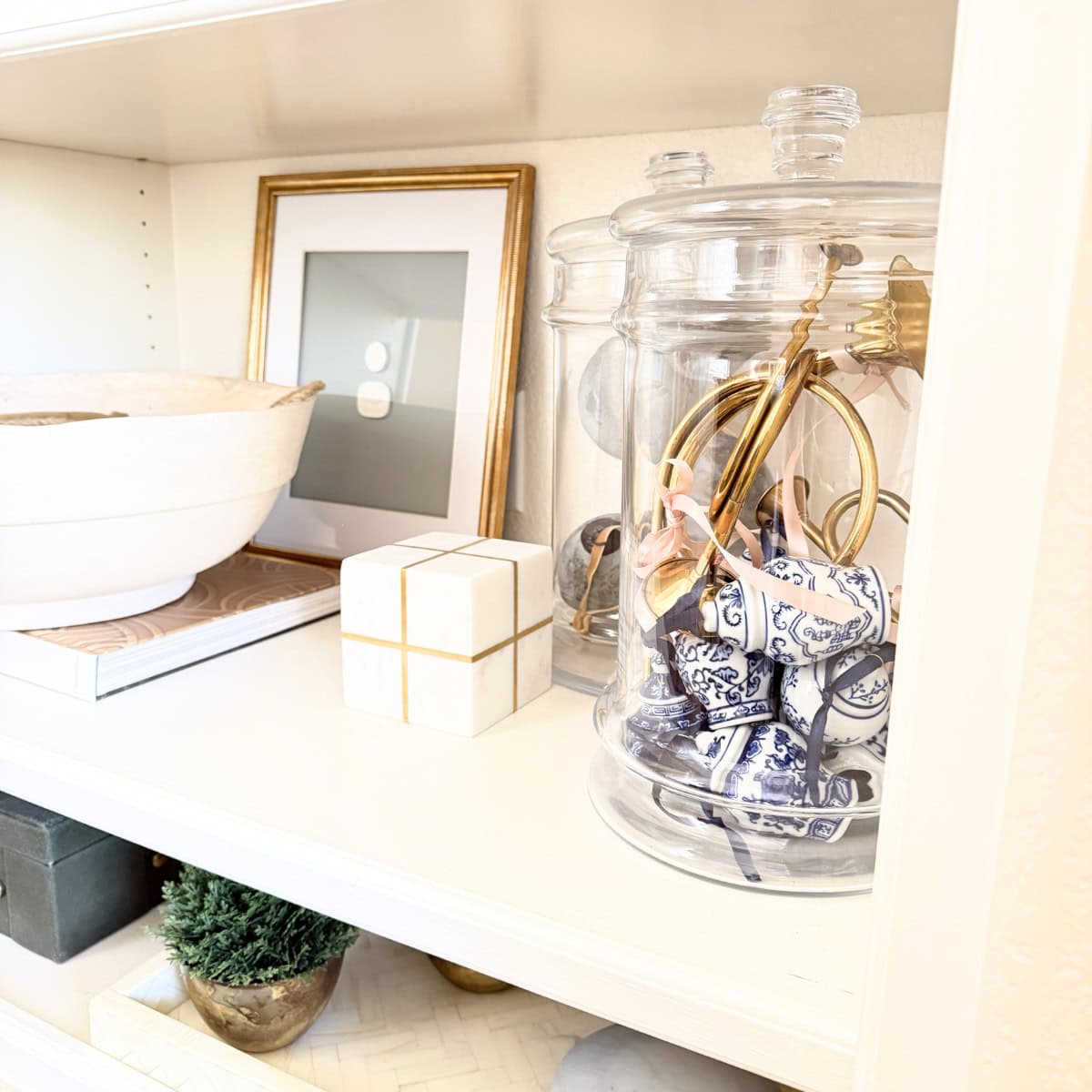 shelf styled with glass jars and leaning artwork and a large paper mache bowl