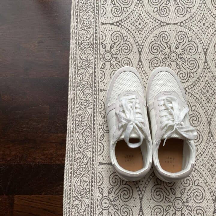 Pair of white and grey women's sneakers on a rug next to dark hardwood floors. Demonstrating using rubbing alcohol to remove shoe scuff marks.