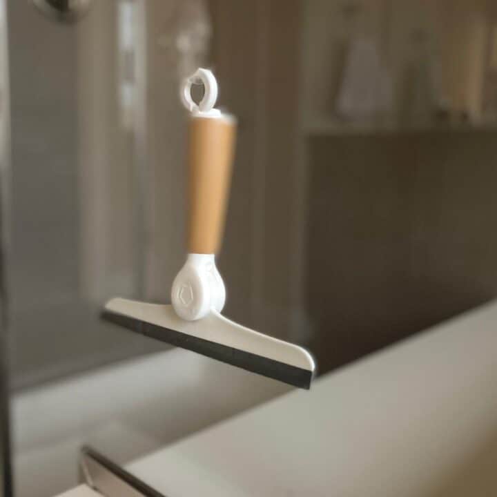 Shower squeegee with a wood handle and white squeegee, suctioned to a glass shower wall.